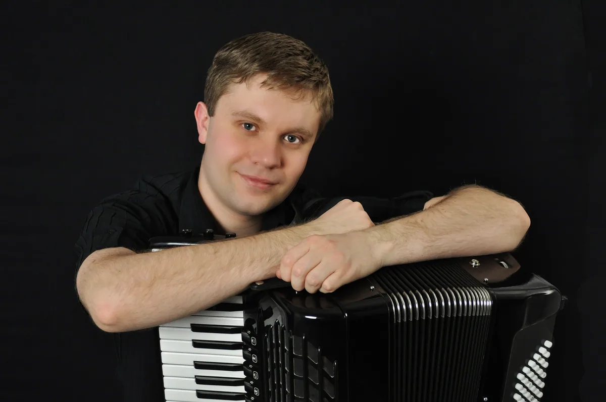 Konstantin Ivanov stützt sich vor schwarzem Grund auf sein Akkordeon