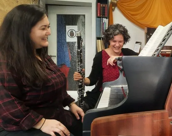 Antje Taubert mit Bassklarinette und eine Pianistin proben lachend am Flügel im Klavierladen