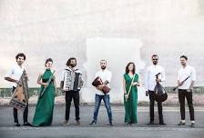 Das Ensemble SYRIAB: Musikerinnen und Musiker mit ihren Instrumenten nebeneinander vor einer hellen Wand