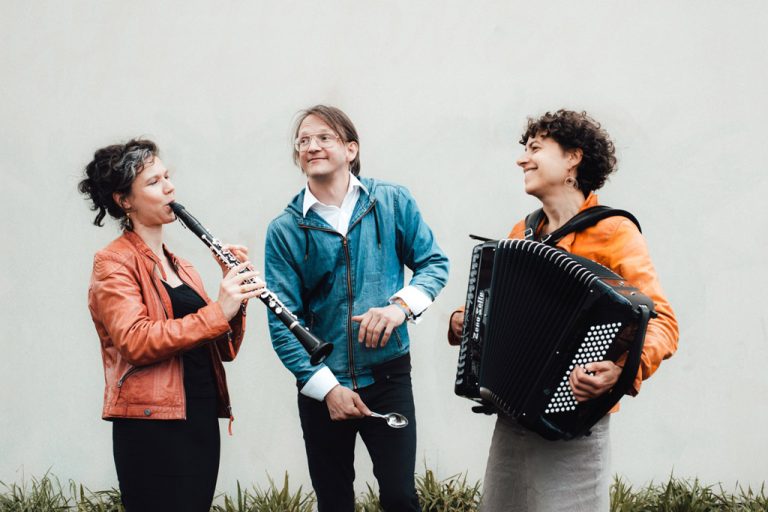 Antje Taubert mit Klarinette, ein Musiker und eine Akkordeonistin vor einer hellen Wand