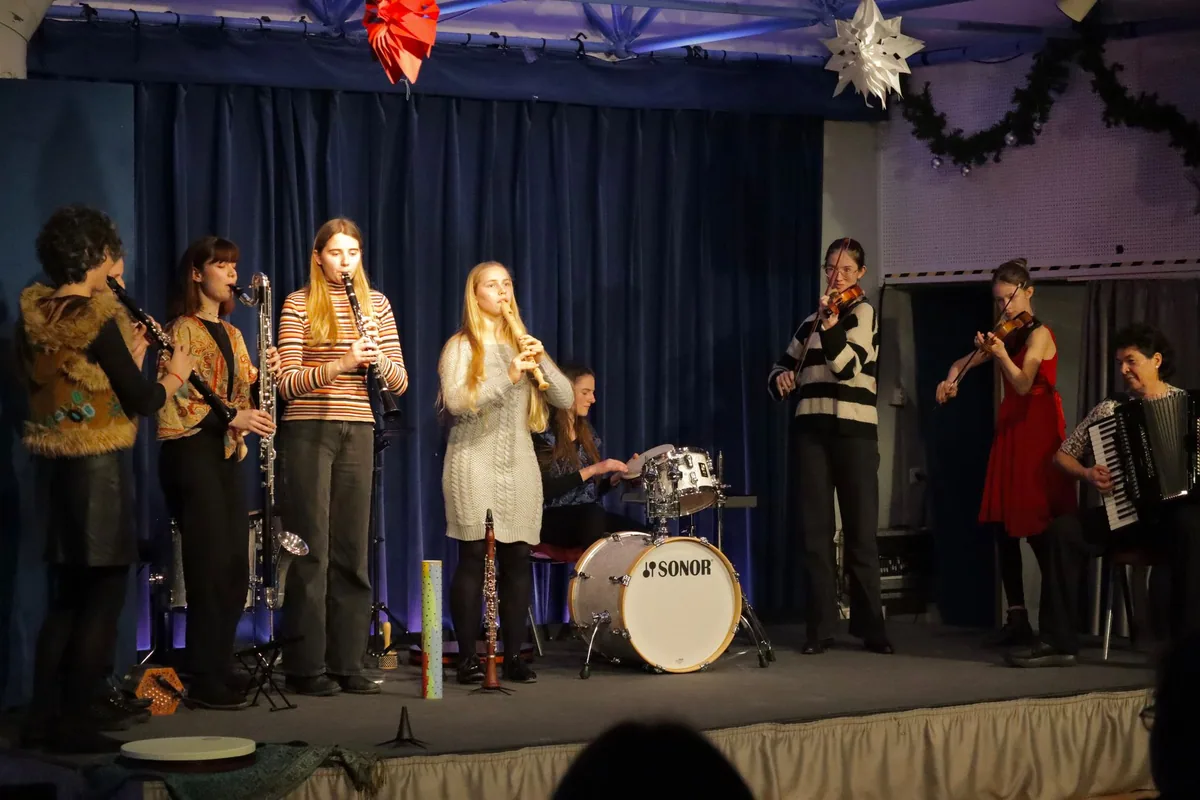 Das Klezmerensemble auf einer weihnachtlich geschmückten Bühne: Klarinetten, Flöte, Geigen, Schlagzeug und Akkordeon