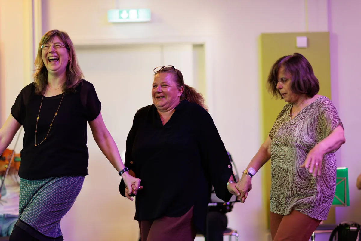 Drei Frauen fassen sich an den Händen und lachen