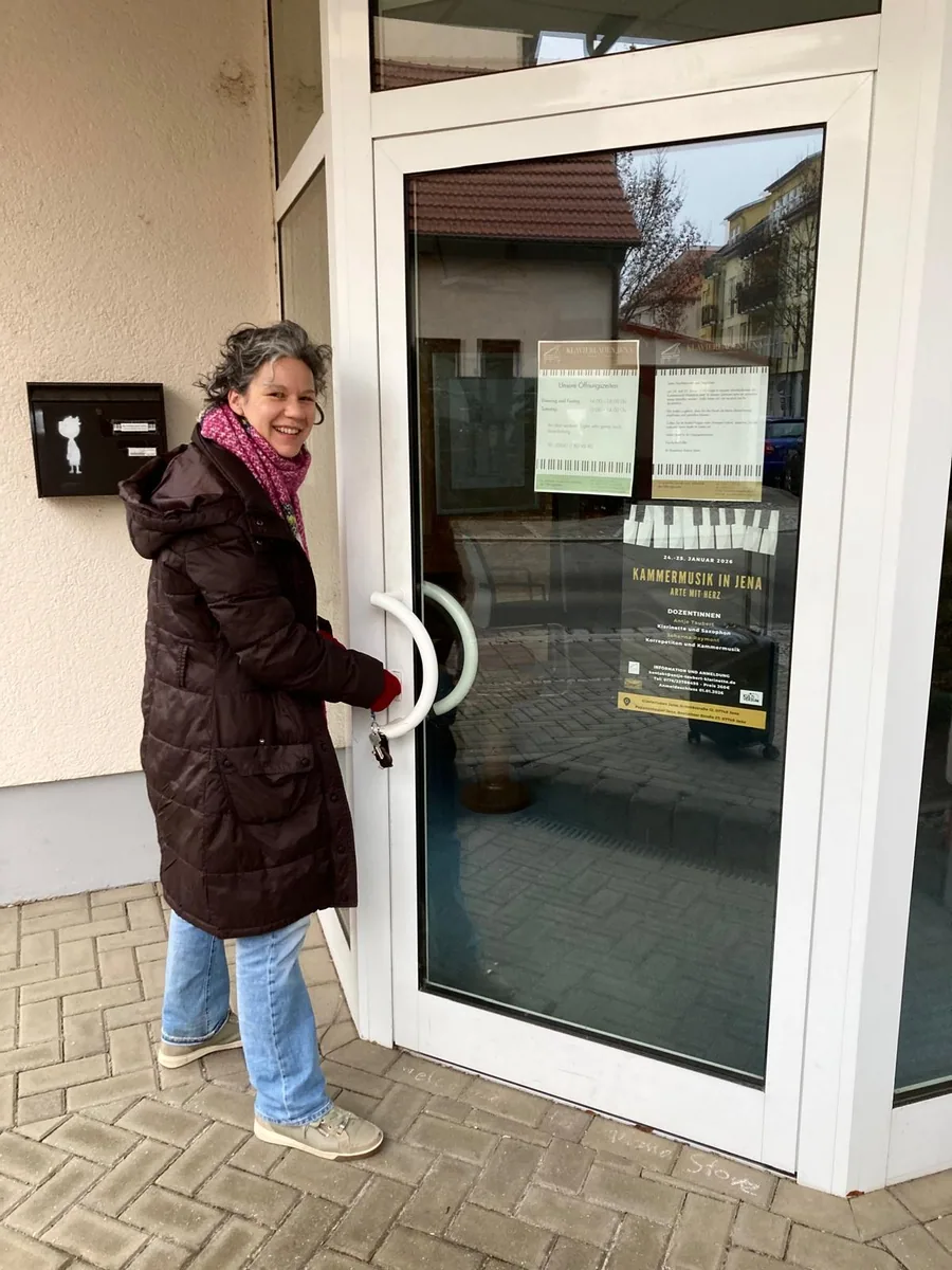 Antje Taubert in Winterjacke öffnet die Glastür zum Veranstaltungsort