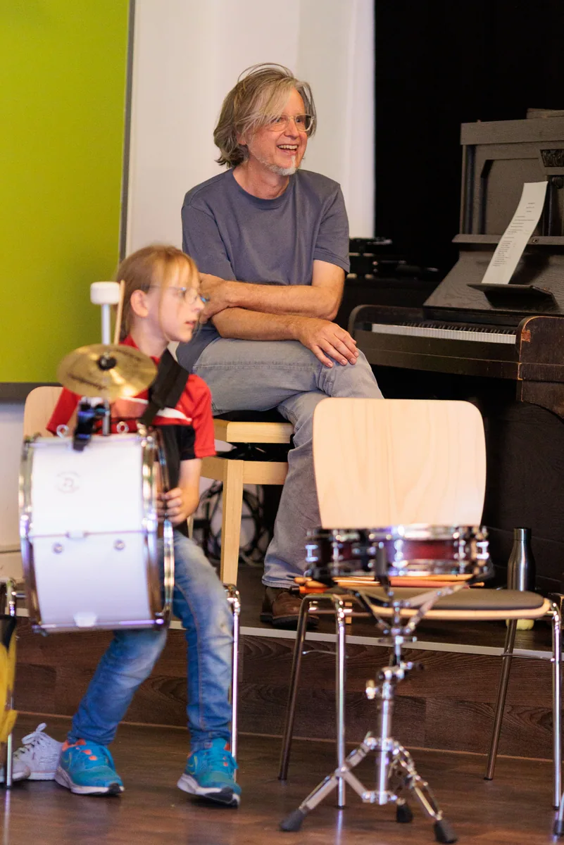 Ein Kind spielt Trommel, daneben lacht der Pianist